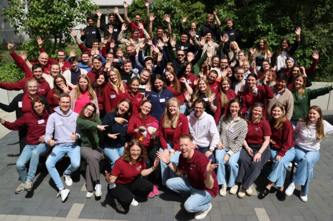 Knapp 70 Menschen auf einem Gruppenfoto jubeln.